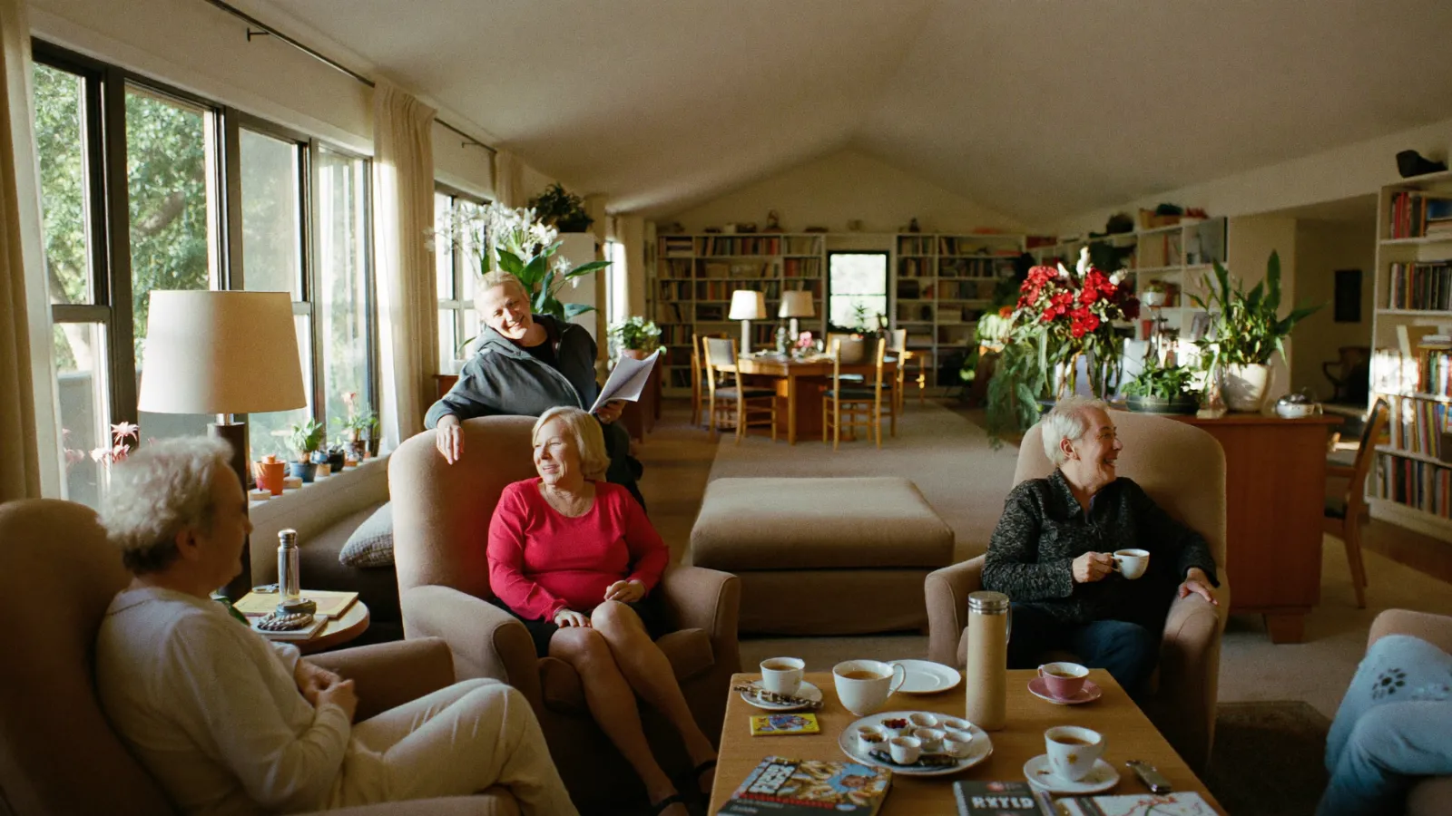 Older adults chatting over tea in armchairs in a warm, home-like adult day center lounge